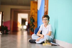 A handsome boy student is sitting on the floor of the school corridor photo