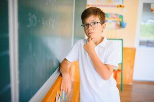 Cute little schoolboy diligent write chalk solve math problem dressed stylish uniform classroom blackboard background photo