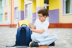 Portrait of a junior high school student sitting and reading a book near the school. Learning concept photo