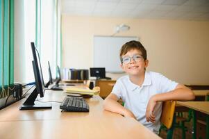 Teenage boy smiling while using computer at desk in classroom photo