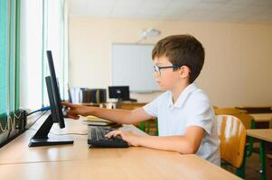 Teenage boy smiling while using computer at desk in classroom photo