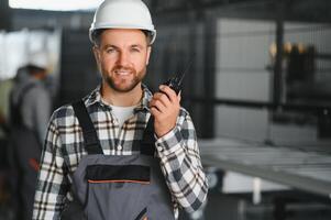 Smiling and happy employee. Portrait of industrial worker indoors in factory. Young technician with white hard hat photo