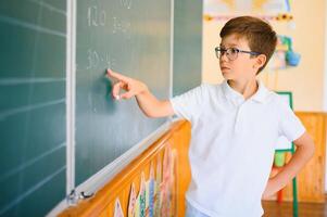 Cute schoolboy near blackboard in classroom photo