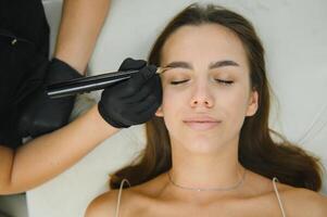 Beauty masters hands do permanent eyebrow makeup. Eyebrow microblading is performed using manipulator handle and special nozzle with needles photo