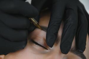 hands of the master who performs the procedure of permanent makeup of eyebrows. Permanent eyebrow makeup PMU for brunettes photo