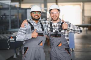 Two happy international workers in overalls hug each other against a factory background photo