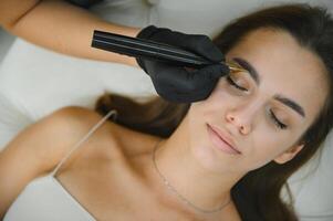 Beauty masters hands do permanent eyebrow makeup. Eyebrow microblading is performed using manipulator handle and special nozzle with needles photo