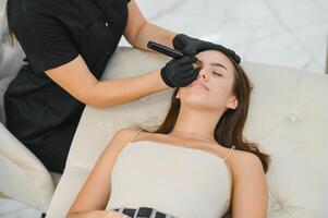 Beauty masters hands do permanent eyebrow makeup. Eyebrow microblading is performed using manipulator handle and special nozzle with needles photo