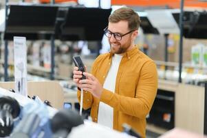 A bearded stylish man makes a choice while standing at a showcase with electronic trimmers and razors photo