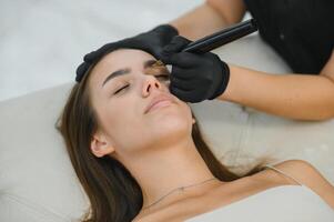 Beauty masters hands do permanent eyebrow makeup. Eyebrow microblading is performed using manipulator handle and special nozzle with needles photo