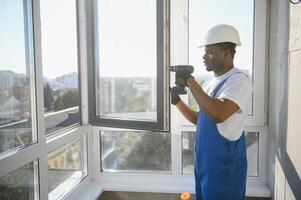 Workman in overalls installing or adjusting plastic windows in the living room at home photo