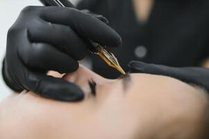 hands of the master who performs the procedure of permanent makeup of eyebrows. Permanent eyebrow makeup PMU for brunettes photo