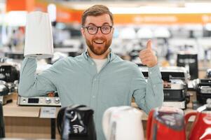 Smart young customer chooses a kettle in supermarket mall photo