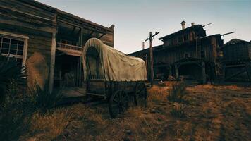 An antique covered wagon in front of a rustic wooden building video
