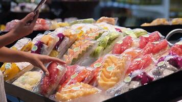 A close-up of a hand holding a smartphone near shelves of fruits, as an unrecognizable woman calculates calories or uses a shopping app. This scene highlights modern healthy living and smart shopping video