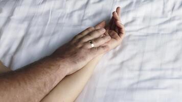 A close-up of a couple's hands intertwined on the bed, capturing a moment of relaxation. This scene conveys the connection and pleasure in their loving relationship video
