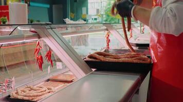 Butchers hands arranging sausages on tray for display cabinet at shop. video