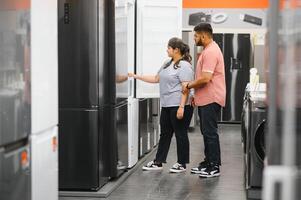 Young indian couple, satisfied customers choosing fridges in appliances store photo