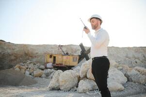 A worker in a helmet stands on the background of an excavator in a quarry photo
