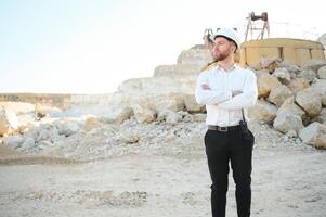 A worker in a helmet stands on the background of an excavator in a quarry photo