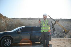 A worker in a helmet stands on the background of an excavator in a quarry photo