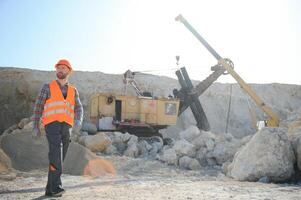 A worker in a helmet stands on the background of an excavator in a quarry photo
