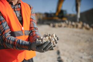 A worker in a helmet stands on the background of an excavator in a quarry photo