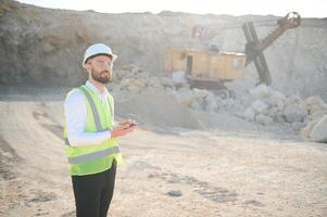 A worker in a helmet stands on the background of an excavator in a quarry photo