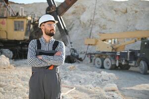 A worker in a helmet stands on the background of an excavator in a quarry photo