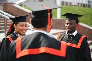 Group of happy smiling multicultural people in graduation gowns and caps with diplomas in hands graduate university outdoors in campus looking at camera. Graduation from college, university concept. photo