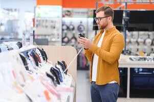 A bearded stylish man makes a choice while standing at a showcase with electronic trimmers and razors photo