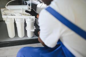 Plumber installs or change water filter. Replacement aqua filter. Repairman installing water filter cartridges in a kitchen. photo