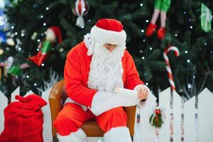 Santa Claus sitting on the background of the Christmas tree in the lobby of the modern shopping mall. Bokeh basic background for design. photo
