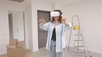 Young woman in VR glasses using modern technology creating room design, moving hands in air, standing in new apartment during renovation. Virtual reality and repair concept video
