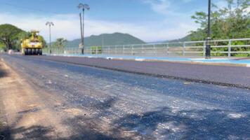 road roller compressing freshly laid asphalt on a road construction site. The yellow roller is seen working on a smooth section of the road, with the surrounding guardrails, civil engineering video