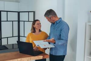 Man and woman smiling professional business people talking using laptop computer working in office. photo