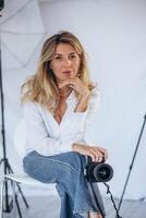 Female photographer holding a camera, standing confidently in a modern studio. A dynamic scene highlighting passion and creativity in photography. photo
