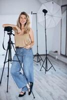 The photo shows a female photographer working in a studio environment. She is surrounded by professional equipment, focusing on capturing the perfect shot in a creative and controlled setting