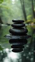 Four smooth stones stacked in serene water surrounded by lush greenery in a tranquil setting photo