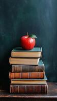 A fresh red apple placed atop a stack of vintage books on a wooden table in a cozy setting photo