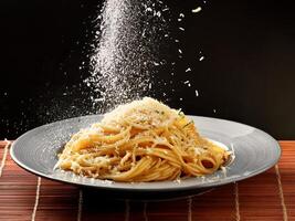 A plate of spaghetti with cheese being sprinkled on it photo