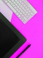 A keyboard, mouse, and tablet on a pink background photo