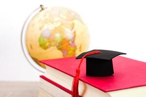 A Graduation cap placed on a stack of books and blurred globe behind. It is the concept of education, knowledge, learning and successful. photo