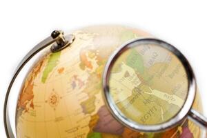 Selective focus, looking the globe through magnifying glass on white background. Learning, study, education and explore concept. photo