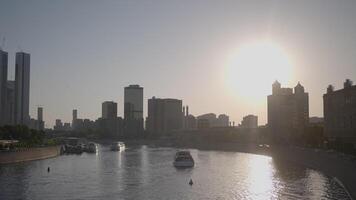 River with boats in modern city on background of bright sun. Action. City canal with floating yachts on sunny day. Modern expensive city with floating yachts on river video