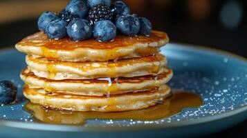 Delicious stack of fluffy pancakes topped with fresh blueberries and syrup served on a blue plate photo