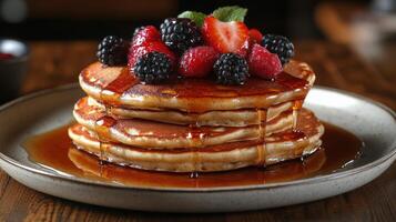Stacked pancakes topped with fresh berries and maple syrup served on a wooden table photo