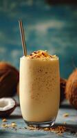 Creamy coconut smoothie topped with crushed nuts served in a tall glass on a blue background photo