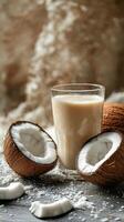 Creamy coconut milk in a glass surrounded by fresh coconuts and shredded coconut on a surface photo