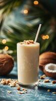Creamy coconut smoothie topped with crushed nuts served in a tall glass on a blue background photo